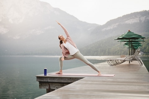 Woman doing yoga on a jetty with beautiful nature surrounding her