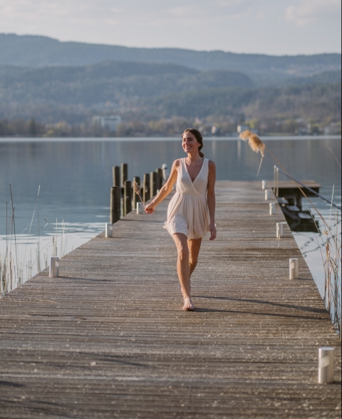 Woman in bright summer dress walking and smiling on private dock at VIVAMAYR Maria Wörth