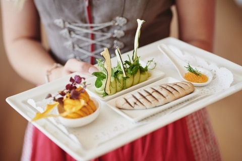 Female waiter in traditional Austrian Dirndl holds a plate with healthy food